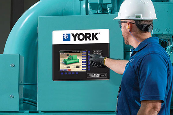 A man standing in front of a YORK industrial chiller talking to two other men