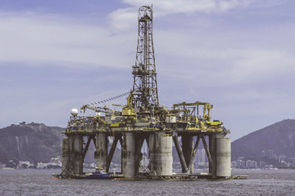 An oil tanker moving towards an oil rig with hills in the background